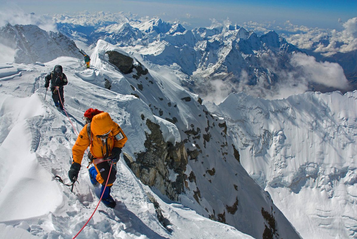 Mountaineer in an orange jacket crossing a snowy ridge