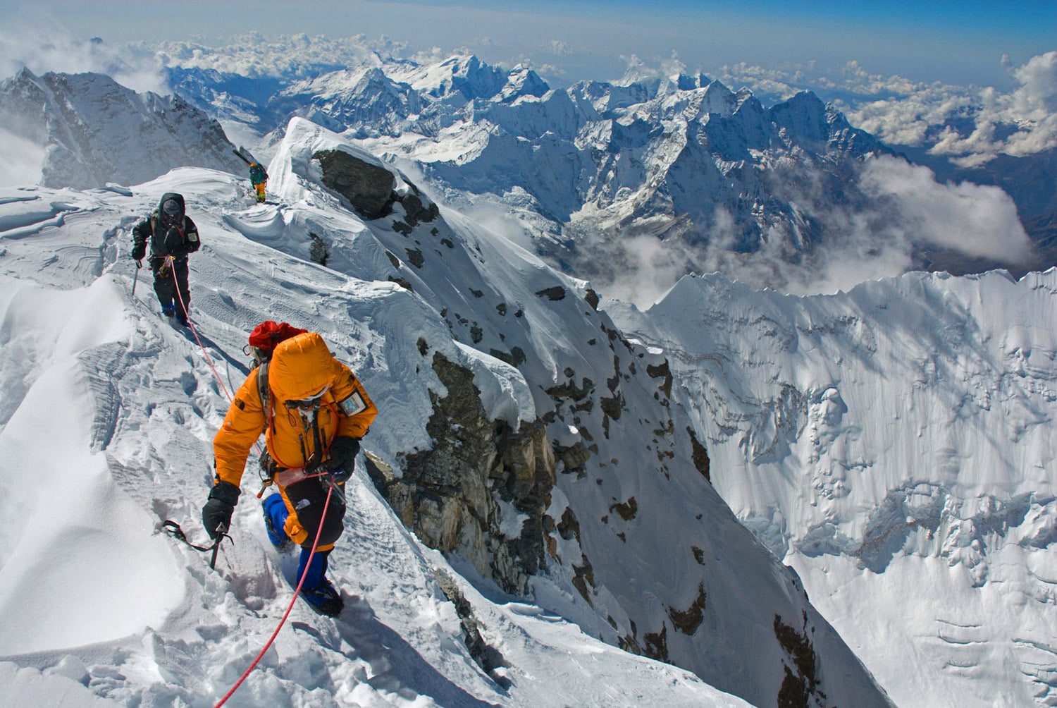 Mountaineer in an orange jacket on a snowy ridge under a clear sky